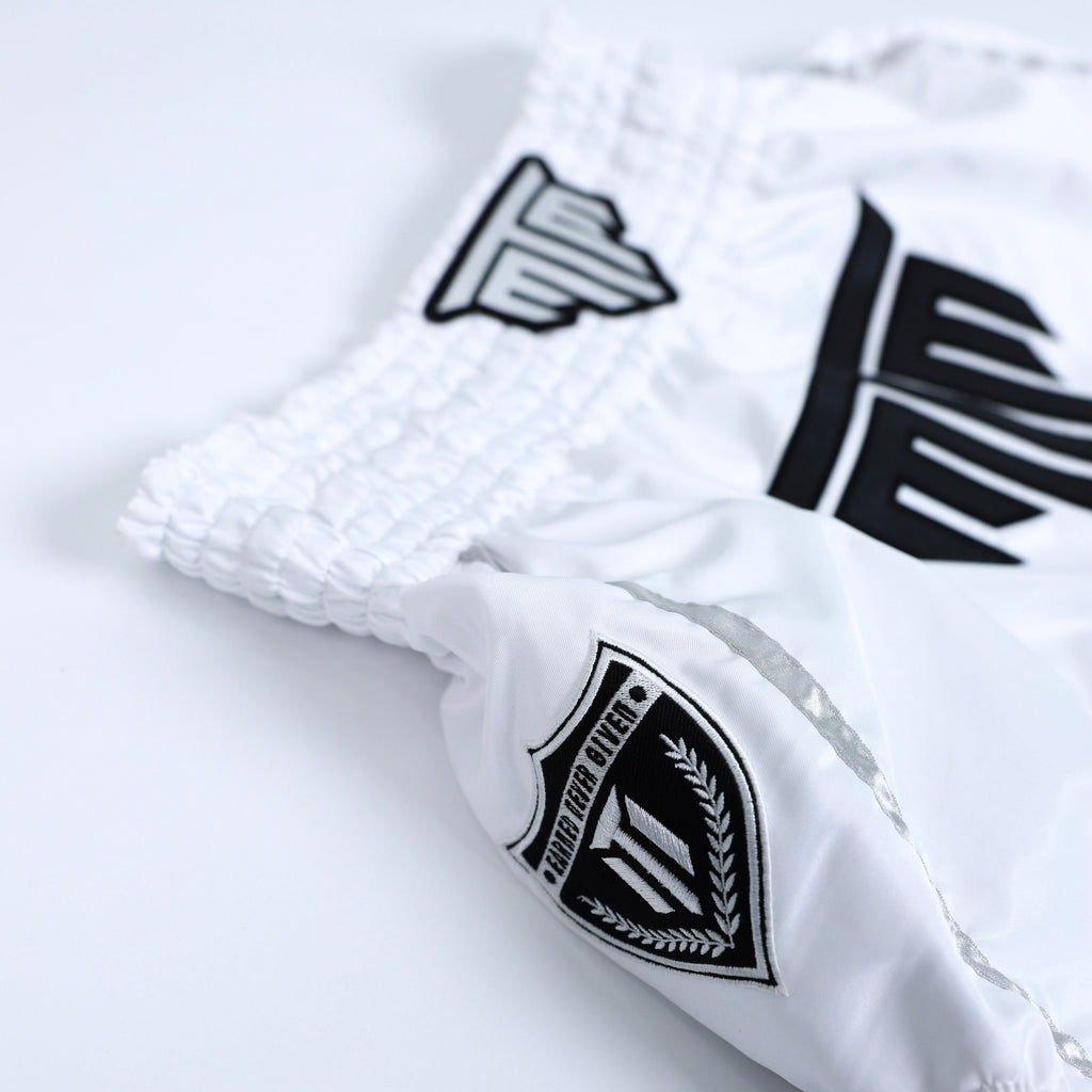 Fighter wearing MTM Essentials Muay Thai Shorts in white, performing a kick