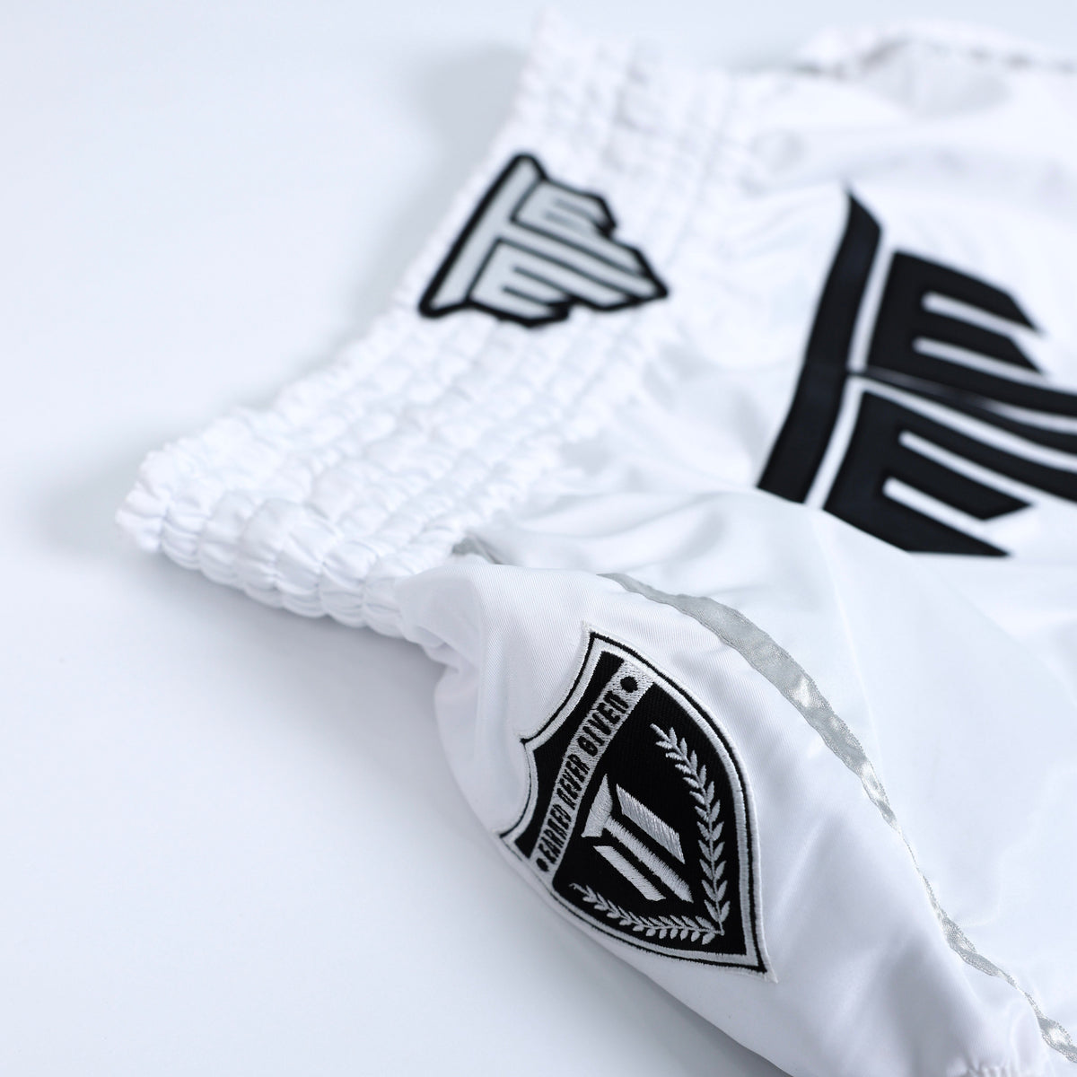 Fighter wearing MTM Essentials Muay Thai Shorts in white, performing a kick